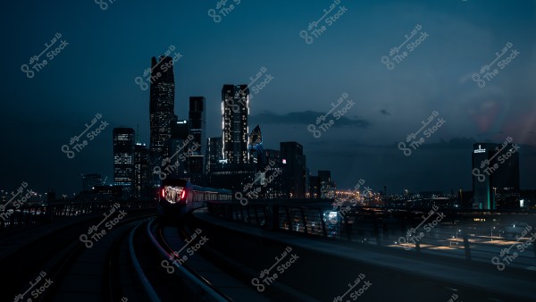 أفق مدينة مضاء في الليل مع قطار يسير على السكة في المقدمة في مدينة الرياض.