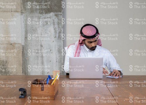 شاب سعودي يعمل بالجهاز المحمول. شاب سعودي يرتدي الثوب يكتب ملاحظات