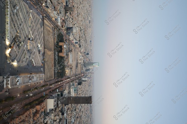 صورة جوية لمدينة الرياض بالمملكة العربية السعودية, تُظهر برج المملكة مع شارع مزدحم بالسيارات. المنطقة المحيطة مليئة بالمباني السكنية والتجارية. السماء صافية ويظهر غروب الشمس في الأفق.