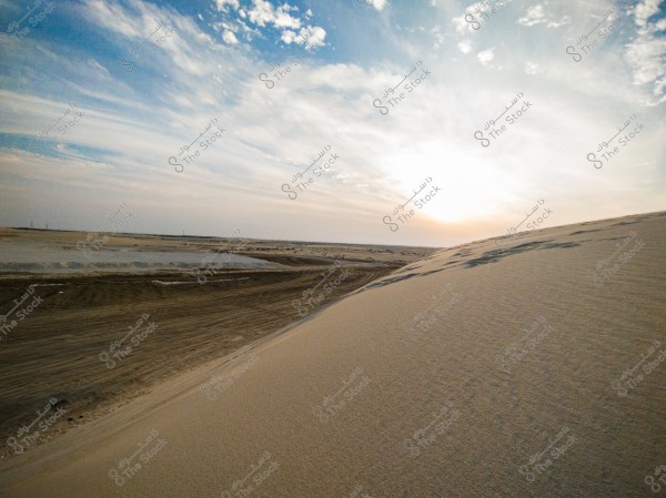 An open desert landscape featuring golden sand dunes under a bright sun on the horizon. The sky is colored in shades of blue and white with intermingling clouds. The horizon stretches far, giving a sense of the infinite expanse of the desert.