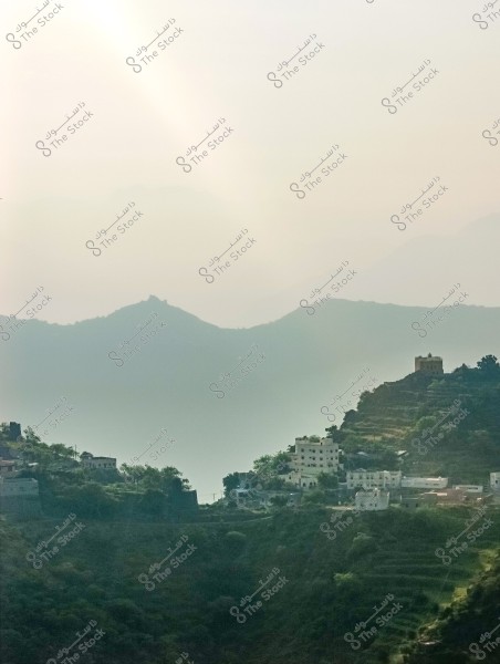 منظر طبيعي يظهر سلسلة من الجبال المتدرجة من محافظة فيفاء بمنطقة جازان جنوب المملكة العربية السعودية في الخلفية مع ضوء الشمس الخافت يعطي جوًا ضبابيًا. في المقدمة توجد تلال خضراء متدرجة تحتوي على بيوت بيضاء تقليدية متوزعة بشكل متناسق, مما يشير إلى قرية جبلية. الألوان تمتاز بالهدوء وطبيعة المشهد تدل على نهاية يوم هادئ.