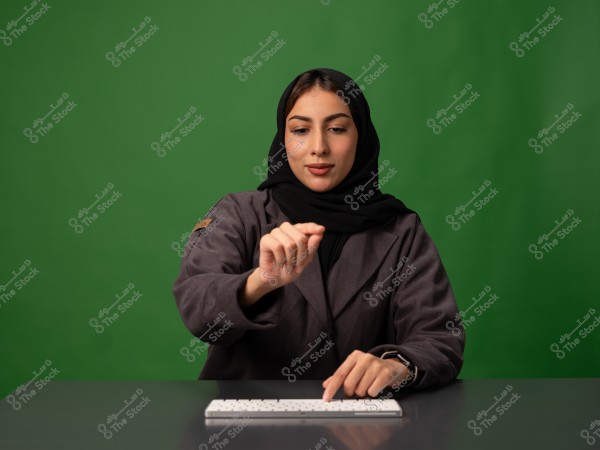 امرأة ترتدي حجابًا تستخدم لوحة مفاتيح أمام خلفية خضراء.
