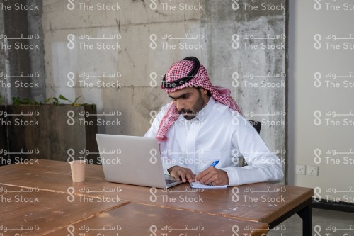 شاب سعودي يعمل بالجهاز المحمول. شاب سعودي يرتدي الثوب يكتب ملاحظات