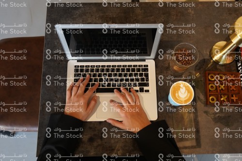 شاب سعودي يعمل ويستخدم جهاز محمول في المقهى وبجابنه كوب قهوة