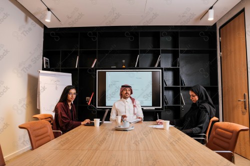 A Saudi man in traditional Saudi dress holds a meeting with Saudi female employees wearing abaya in the meeting room