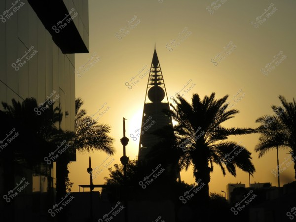 Image showing a sunset scene behind the Al Faisaliah Tower in Riyadh, Saudi Arabia. The tower is prominent with its distinctive peak and large glass sphere. Palm trees stand silhouetted in the foreground, while the golden sunlight reflects off the glass building on the left side of the photo, adding a magical touch to the scene.