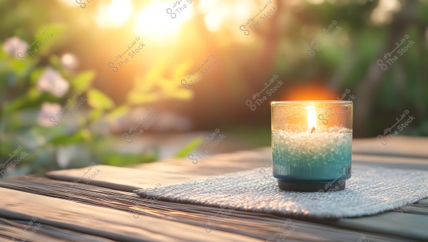 An image of a lit candle flame inside a glass cup with blue and white colors, placed on a wooden table outdoors. The composition suggests a sense of calmness and tranquility amid nature, enhanced by the soft sunlight in the background and blurred foliage.