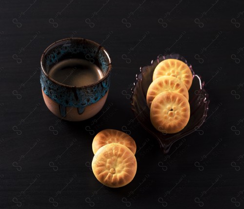 Close-up of a cup of hot black coffee and a plate of maamoul on a wooden table. Snack.