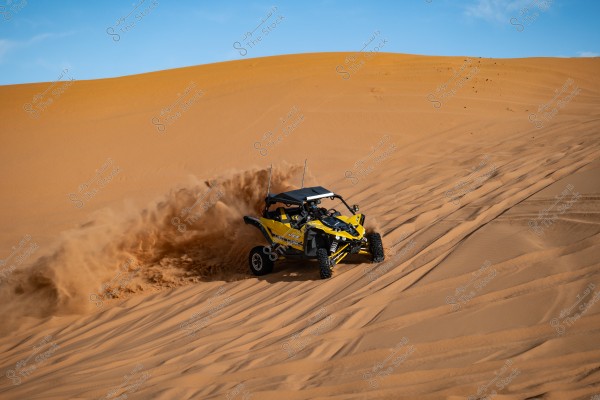 A yellow racing car speeding on sand dunes in the desert, leaving a cloud of sand behind. The sky is blue and clear, reflecting excitement and adventure in an open desert environment.