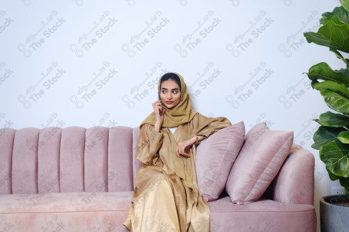 A Saudi girl sitting on the sofa and making different expressions using a mobile phone