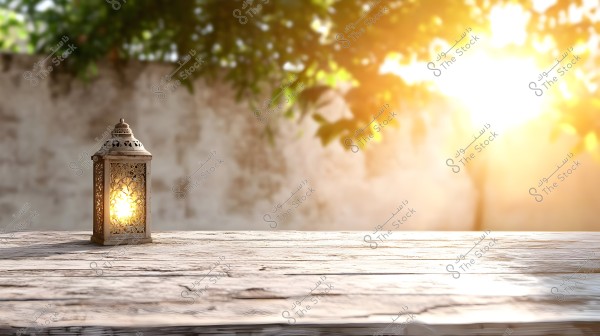 A lit metal lantern with traditional designs on a wooden surface, with a blurred wall and angled sunlight with green leaves in the background.