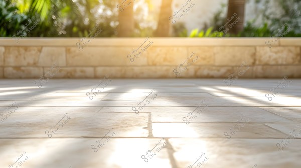 Image showing a light-colored, modern tiled floor with a low stone wall in the background. Sunlight filters through tropical trees and plants, which are blurred in the distant background. The image is characterized by bright natural lighting, giving a warm feel.