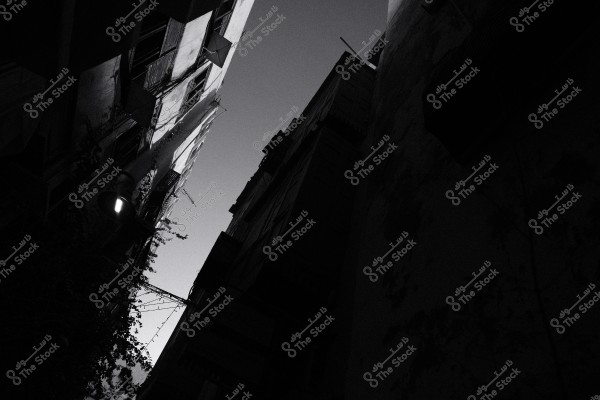 صورة بالأبيض والأسود لمباني مرتفعة في زقاق ضيق مع سماء مظلمة في الخلفية.