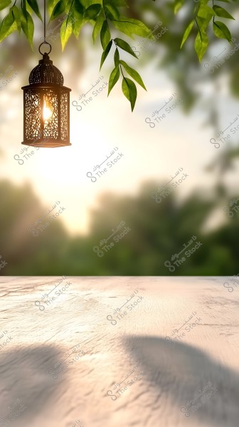 Image of a traditional metal lantern with intricate designs hanging among tree branches, with a blurred background of green trees and a soft sunlight glow in the horizon. The wooden surface in the foreground reflects soft shadows of the lantern and leaves.