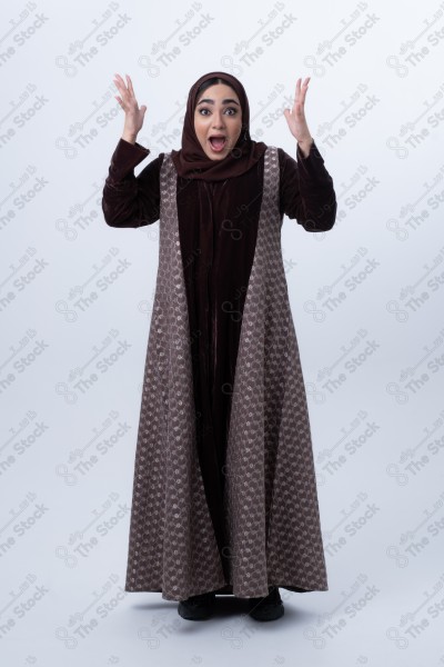 Portrait of a young Saudi woman wearing an abaya and hijab, with a smiling facial expression, standing against a white background