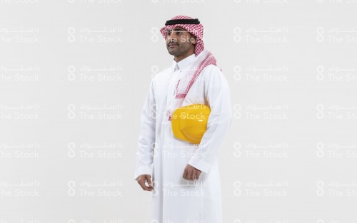 بورتريه مهندس سعودي يحمل خوذة المهندسين على يديه ويرتدي الزي السعودي الرسمي على خلفية بيضاء