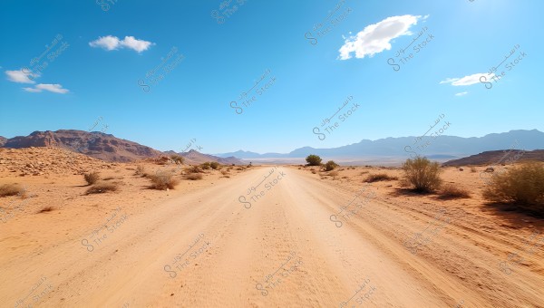 A desert road stretches towards the horizon under a clear blue sky. The image shows sandy hills and small mountains on both sides, with scattered green shrubs along the road.