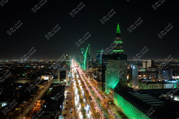 Night view of Riyadh city in Saudi Arabia, showcasing tall buildings illuminated with bright green lights along a busy street filled with cars. The spire-like tower in the foreground and the distinct tower with the gap at the top are clearly visible, highlighting Riyadh\'s unique skyline. The lights stretch into the horizon, giving a sense of vibrancy and motion.