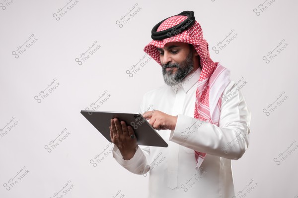 رجل يرتدي الزي التقليدي السعودي ويستخدم جهاز لوحي.