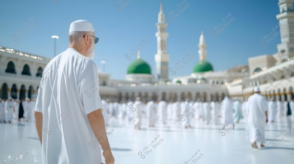 The image shows a person in a white thobe and sunglasses walking in the courtyard of the Prophet\'s Mosque in Medina. The green domes and minarets are visible in the background, with people spread throughout the courtyard wearing similar clothing.