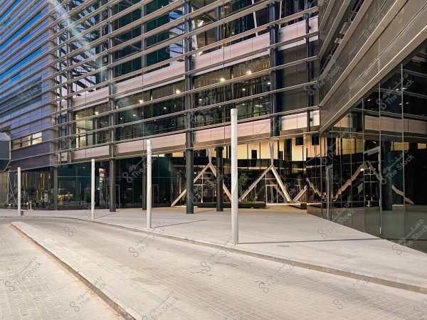A modern building with a glass façade, prominently featuring a metal and steel structure. The road in front of the building is paved and lined with light poles.