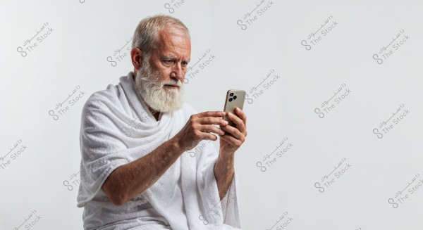 Image of an elderly man with a white beard looking at a smartphone. The man is wearing Ihram clothing, consisting of two pieces of white cloth, typical for Umrah or Hajj. The background is plain white, highlighting the details of the scene.