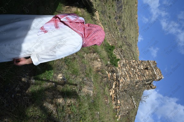 A shot of a Saudi man wearing the Saudi dress, meditating and standing on one of the green mountains.