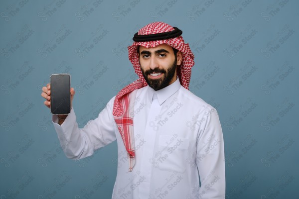 بورتريه شاب سعودي يرتدي الزي السعودي يشير إلى هاتفه ويتفاعل معه، وتظهر على ملامحه الدهشة ، على خلفية سماويه