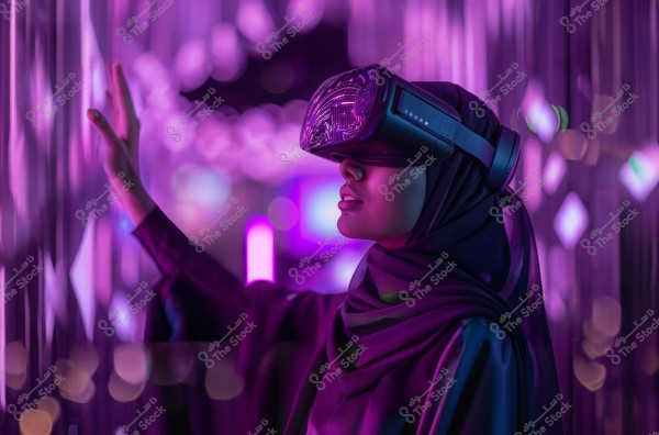 Image of a woman wearing a hijab and virtual reality goggles, surrounded by a luminous environment with purple and blue colors. The woman has her hand raised as if interacting with an unseen element in her surroundings. The image may originate from a Middle Eastern country given the hijab.