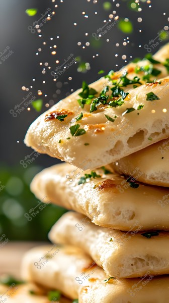 An image of slices of fresh bread stacked on top of each other, topped with fresh parsley pieces. The bread appears golden and crispy with bubbly details from baking. The background is dark with scattered sparkling lights.