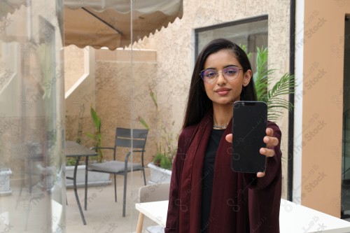 A Saudi woman wearing an abaya holds a mobile phone and displays its screen