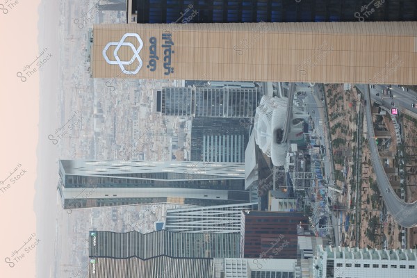 مشهد عام لمدينة حديثة مع أبراج شاهقة, يظهر أحد المباني البارزة بشعار مرئي, ومن حولها شوارع ومباني أخرى متنوعة. في الخلفية يمكن رؤية منظر المدينة المتسع مع الطرق والسيارات.