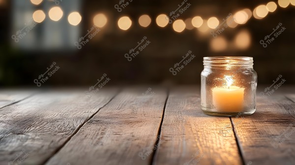 A lit candle placed inside a glass jar on a wooden table. In the background, soft lights add a warm and cozy touch to the scene.