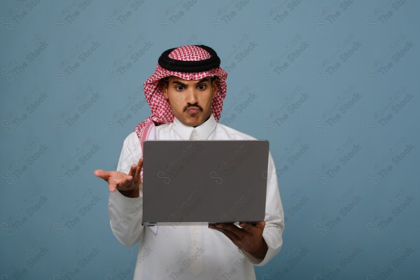 بورتريه شاب سعودي يرتدي الزي السعودي ينظر إلى جهاز المحمول وتظهر على ملامحة التعجب ، يقف على خلفية سماوية