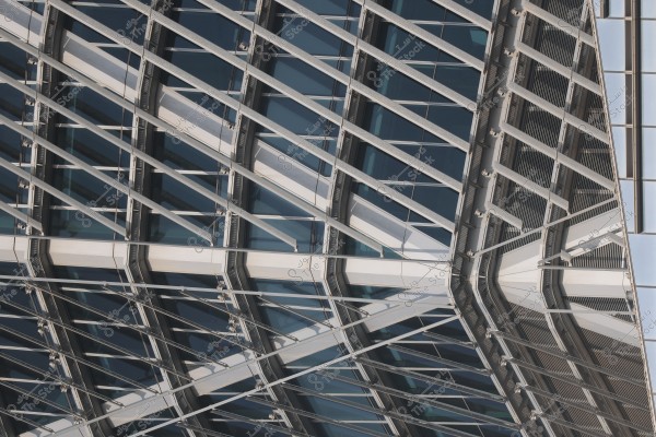 Image showing a modern glass facade of an architectural building with a distinctive geometric design, consisting of large glass panels supported by intersecting metal frames at angular positions.