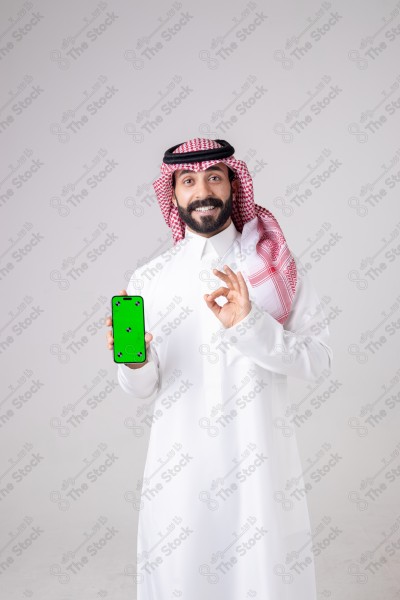 Portrait of a Saudi man holding a phone, pointing at the phone and making different expressions - green screen