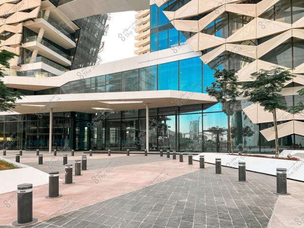 A modern building with a unique architectural design featuring blue glass and interlocking geometric facades. The front entrance is visible with pillars and plants surrounding the area, and the flooring consists of gray and pink tiles.
