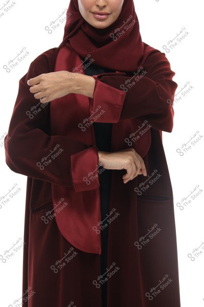 صورة لامرأة ترتدي حجابًا باللون الأحمر الداكن وعباءة متناسقة اللون. تُظهر الصورة الجزء العلوي من جسدها وهي تقوم بتعديل كم العباءة.