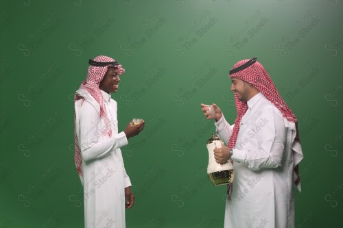 رجل سعودي يرتدي الثوب و الشماغ يقوم بسكب القهوة السعودية لرجل اخر وهما سعيدان