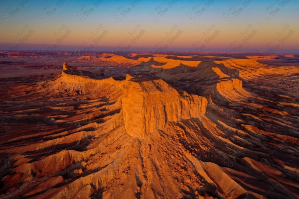 An aerial shot of the Tuwaiq mountain range in the Najd region, showing the sky in Portuguese color during the day, a series of rocky mountains, the edge of the world.