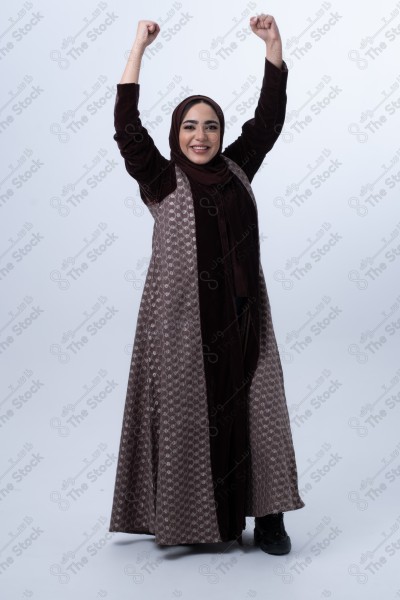 Portrait of a young Saudi woman wearing an abaya and hijab, with a smiling facial expression, standing against a white background