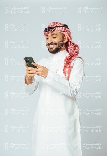 بورتريه رجل سعودي يرتدي الزي السعودي التقليدي يستخدم الجوال وينظر للشاشة بينما يتصفحه