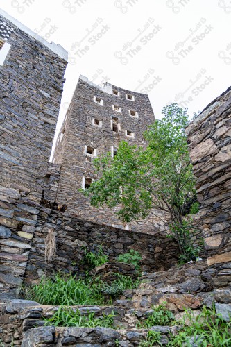 An ancient building built of medium stones, windows surrounded by white paint while the sky looks cloudy at sunset, Rijal Almaa heritage village in the Asir region