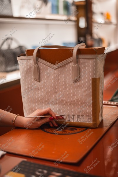 امرأة تقوم بتزيين حقيبة قماشية بحروف محددة في متجر فاخر.