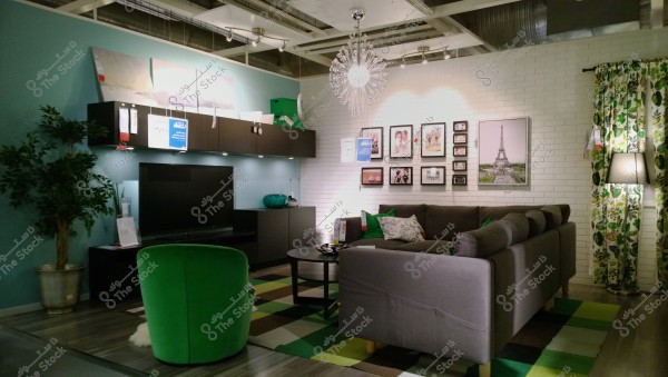A modern living room with a large gray corner sofa adorned with green and white cushions. In the center, there is a round black coffee table accompanied by green seating and a blue glass vase. On the left side, there\'s a sleek black TV storage unit with a decorative indoor plant. The white brick back wall features an art gallery of frames, including a picture of the Eiffel Tower. The lighting includes a modern crystal chandelier and a floor lamp next to green and white patterned curtains.
