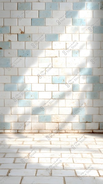 An image of a wall made of white tiles with some light blue tiles, creating a contrasting pattern. The tiles have some spots and discolorations, indicating age or use. There are also patches of light and shadows adding depth and detail.