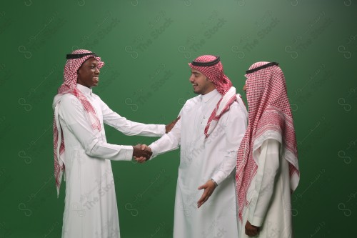 Portrait Saudis men in traditional uniform on a green background shaking hands smiling, sad, angry, memorial photos, documenting a happy moment.