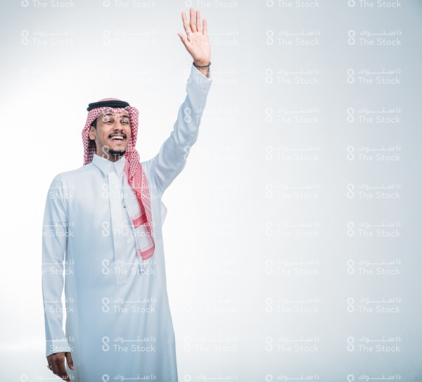 بورتريه رجل سعودي يرتدي الثوب ويقف أمام خلفية بيضاء، يتفاعل بحركات تعبيرية بيديه, يرفع يده للأعلى ، يلقي التحية ويسلم على الآخرين ، توديع الآخرين