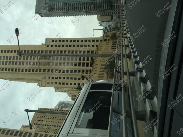 View of a modern city featuring tall buildings on either side of the road. There is noticeable traffic with a bus driving close to the curb and a protective barrier. The buildings have a modern design with multiple windows, and there are road signs and streetlights present.
