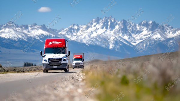A large white truck is driving on a rural road with a backdrop of snow-covered mountains under a clear blue sky. Another truck appears behind the first, both sharing a red cabin top with a white logo. The surrounding landscape enhances the beauty of the mountainous scene.